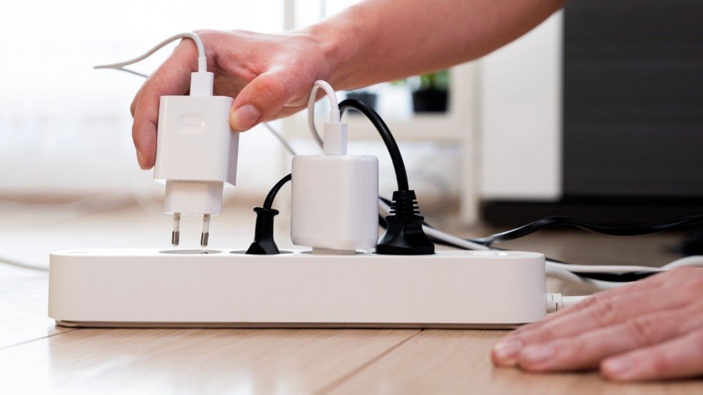 Electrical safety media - hands plugging white USB charger into overloaded white extension lead with multiple chargers